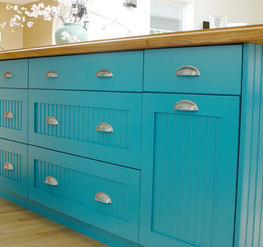 Bright aqua blue cabinets with cottage style cabinet doors on a long kitchen island showing a mix of slab drawer fronts and 5-piece drawers.