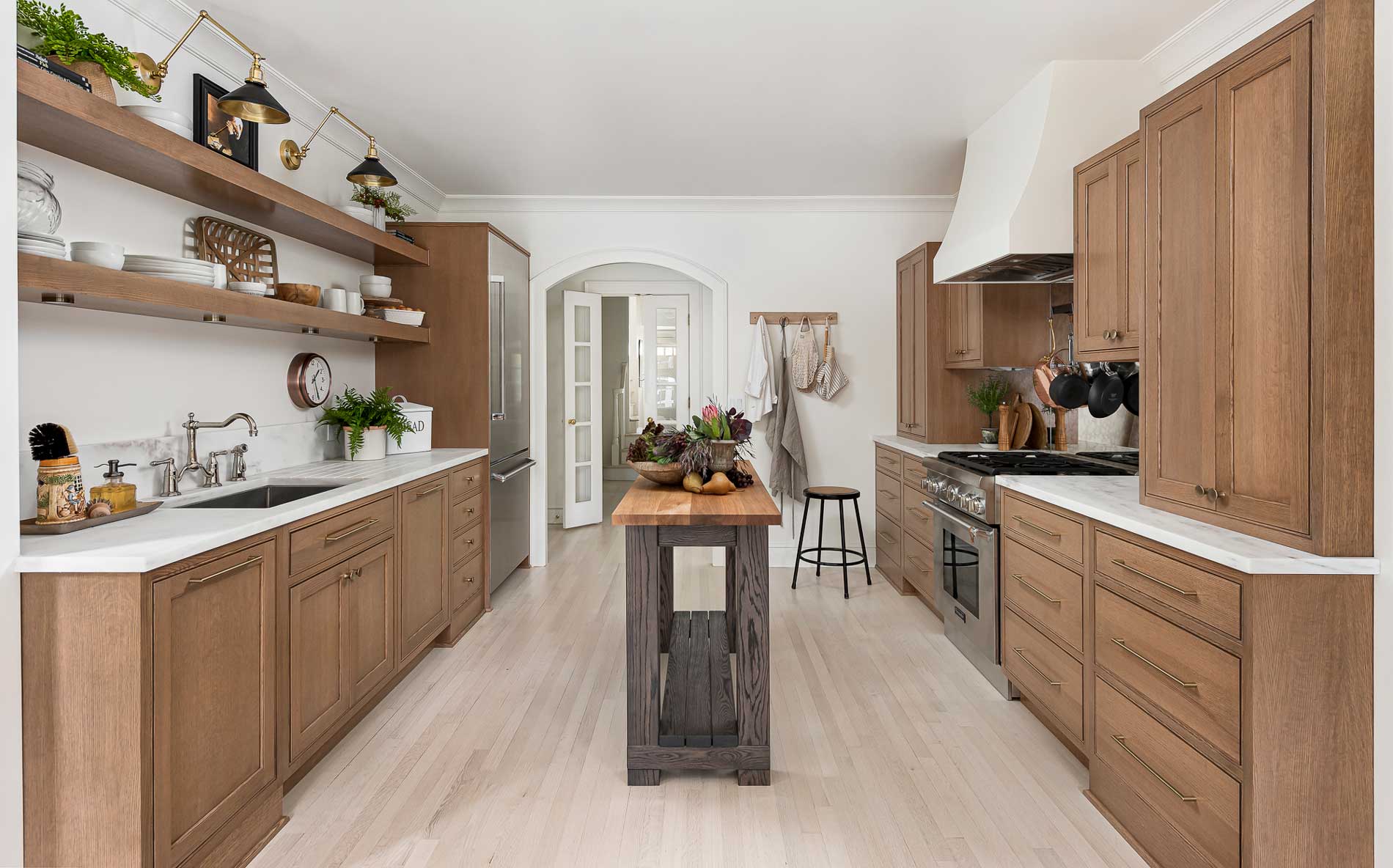 A Danish styled kitchen with inset cabinets in a light stained oak and a tiny kitchen island featuring hidden panel-ready appliances.