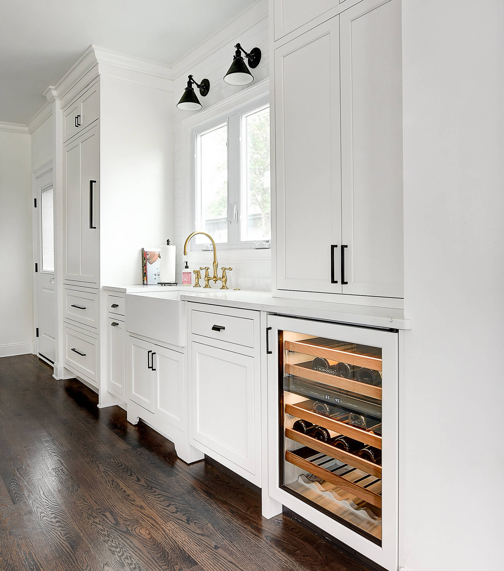 The wall with the sink in this kitchen has a beautiful window view, lots of counter space on both sides of the sink, tons of cabinet storage, and a below counter beverage fridge at the end nearest the dining space.