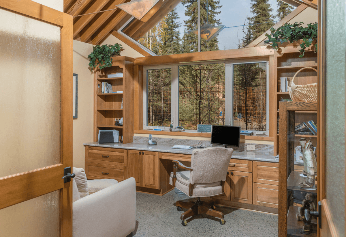 A lovely built-in home office resides in front of a window with a gorgeous view of the outdoors. The home office is designed by Hollie M. Ruocco, CMKBD of Creative Kitchen Designs, Inc featuring Dura Supreme Cabinetry in the Chelsea door with Hickory Butternut finish.