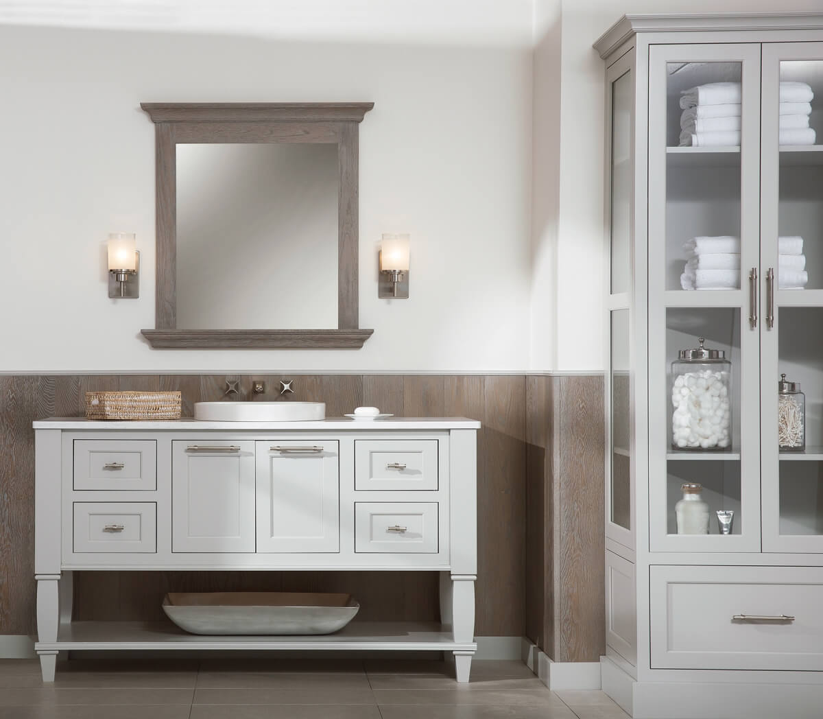 Transitional style bathroom featuring Dura Supreme Cabinetry's furniture vanity style five in the Kendall Panel (inset) door style with Sliver Mist paint finish. Mirror and paneling in a contrasting Weathered Finish 