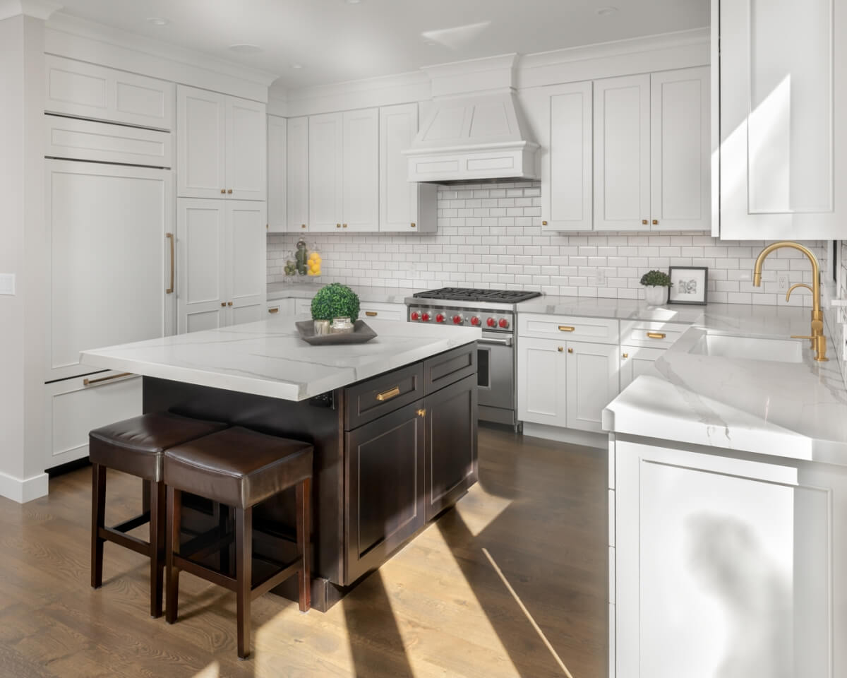 A new kitchen remodel with white painted cabinets, a black kitchen island, gold hardware, and coordinated white quartz countertops that match the cabinetry colors well.