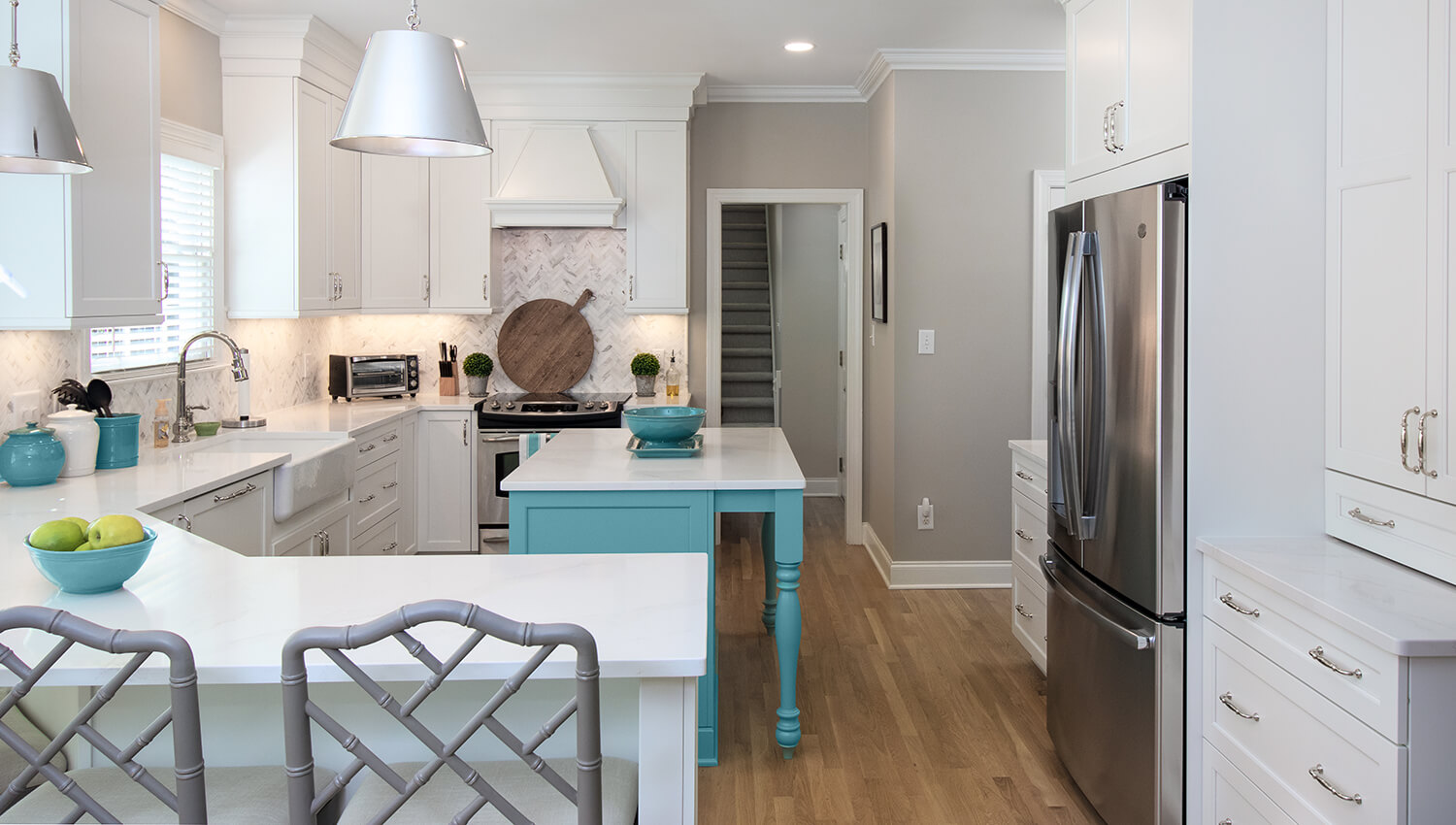 A bright white kitchen with a bright aqua blue kitchen island and a kitchen peninsula for extra seating.