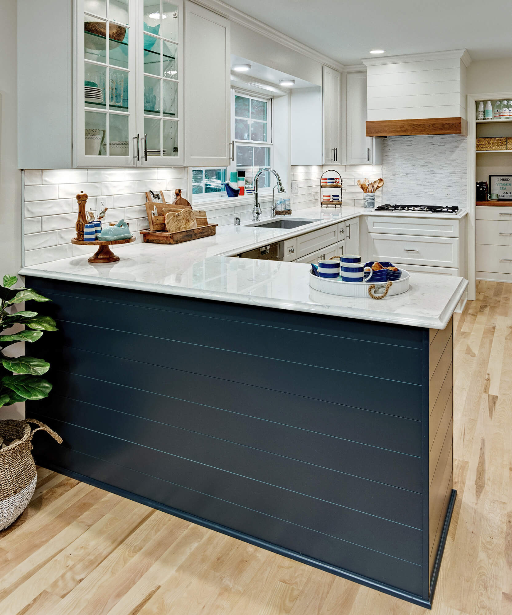 A long kitchen layout with white cabinets and a navy blue peninsula with shiplap details.