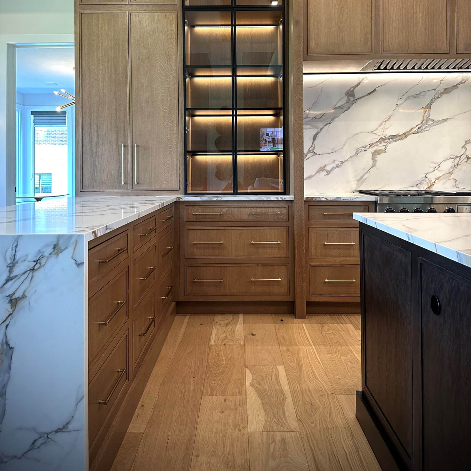 A quarter-sawn white oak kitchen with black metal framed glass doors and a long kitchen peninsula with a waterfall style countertop.