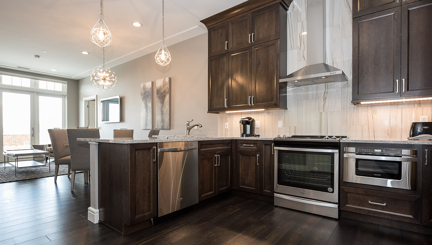 An L-shaped kitchen design in a luxury apartment/condo with dark stained wood cabinets and a kitchen peninsula.