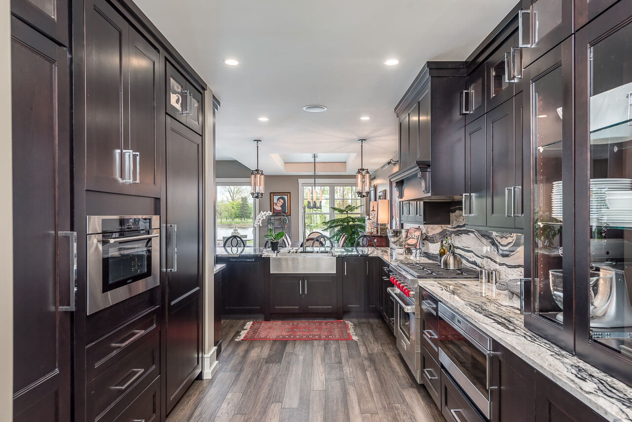 A dark kitchen with black stained cherry cabinets from Dura Supreme Cabinetry and beautiful black and white granite countertops.