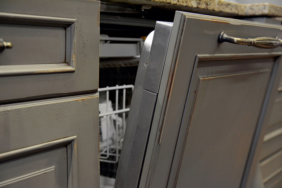 A hidden dishwasher concealed by a paneled appliance cabinet door with a distressed paint finish. This rustic kitchen design has a functional clean-up work station near the kitchen sink.