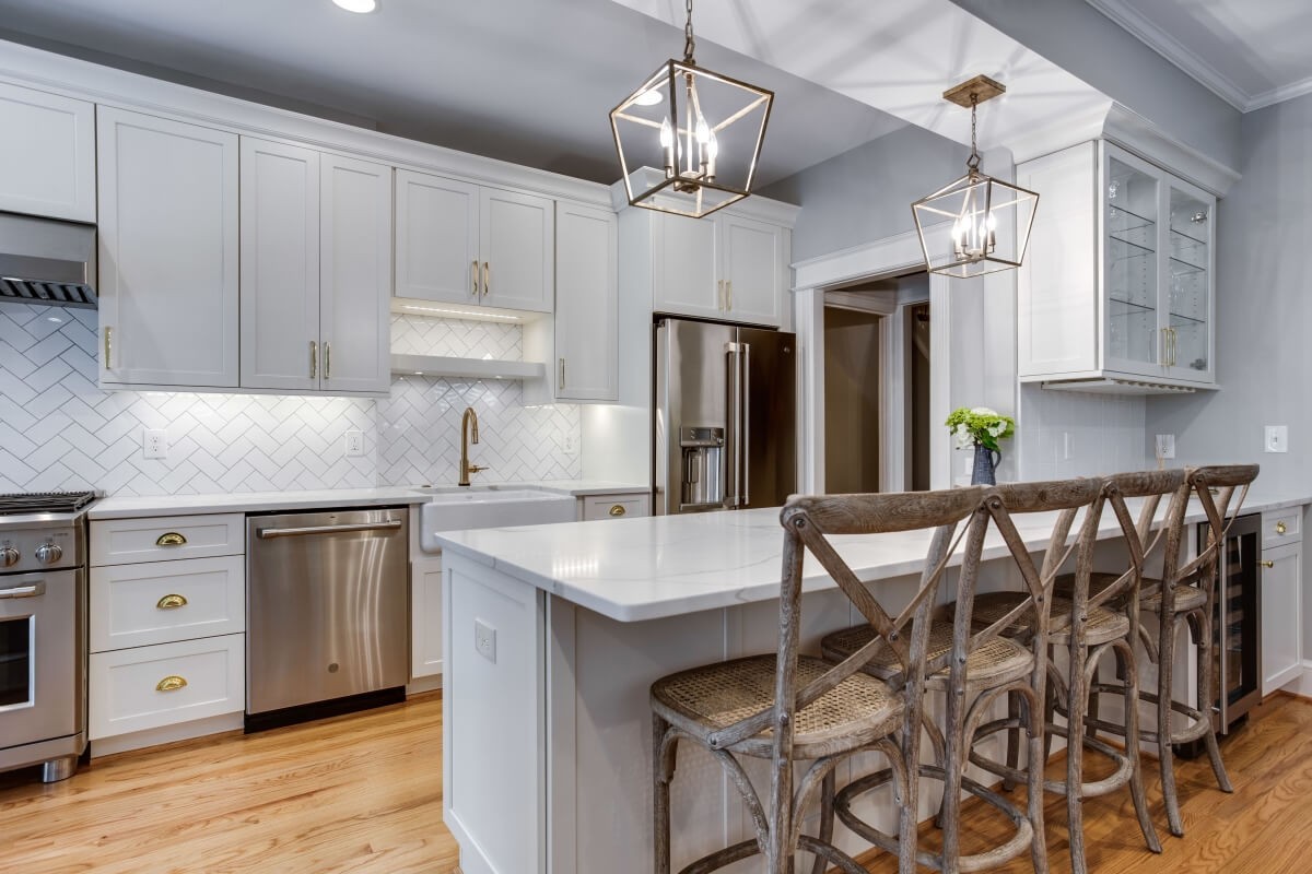 An all white kitchen with white painted cabinets, a long kitchen peninsula, a galley kitchen layout with white countertops and gold hardware.