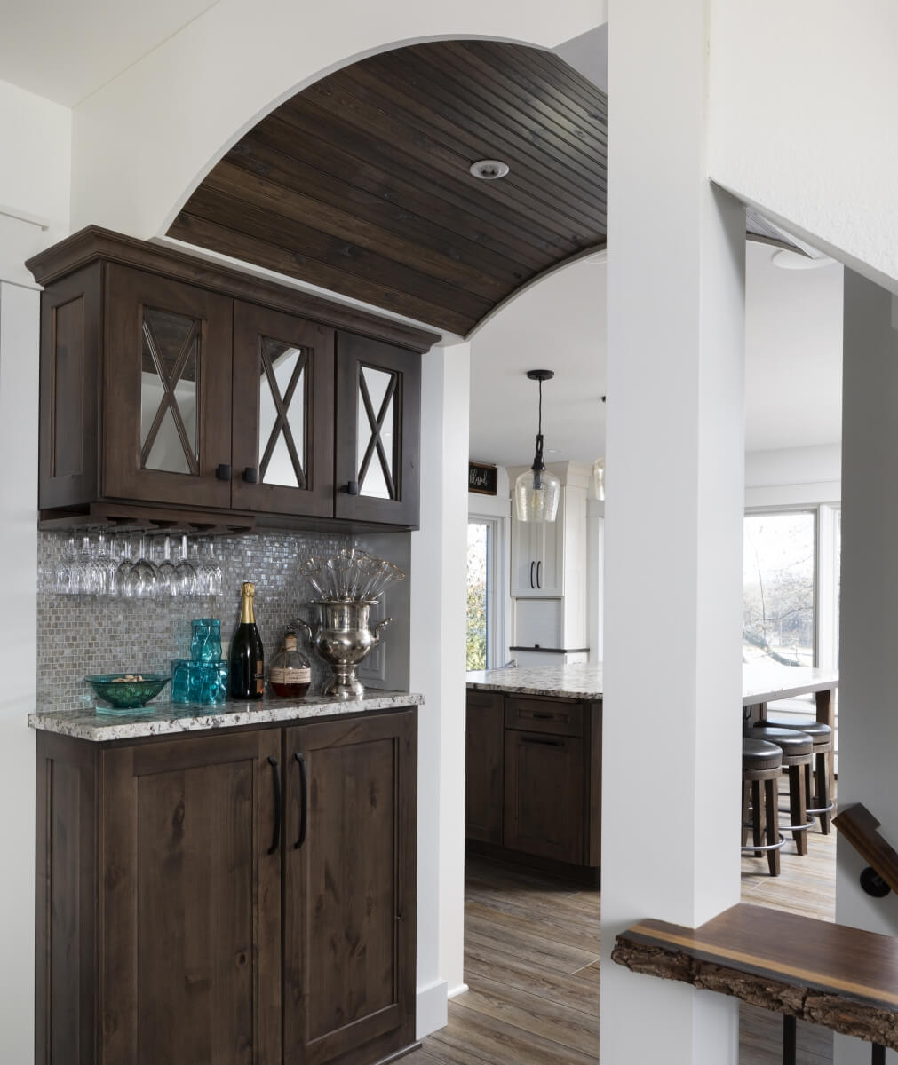 A beautiful hallway with a wet bar, mirrored cabinet inserts, and a barrel ceiling design.