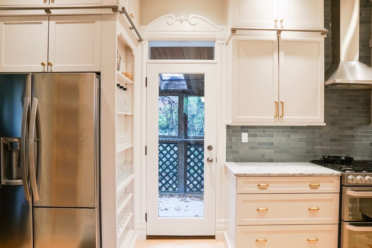 A view out the kitchen door showing the tall thin cabinet on the side of the fridge with open shelves for storage for cups, wine glasses, spices, canned goods and more.