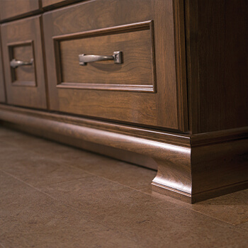 The decorative toe detail on a furniture style vanity cabinet in a master bathroom remodel. The medium stained cherry wood cabinets are warm and inviting. With such an enticing array of options, it’s no wonder Dura Supreme cabinetry has such a broad appeal and application at so many price points and within so many design themes.