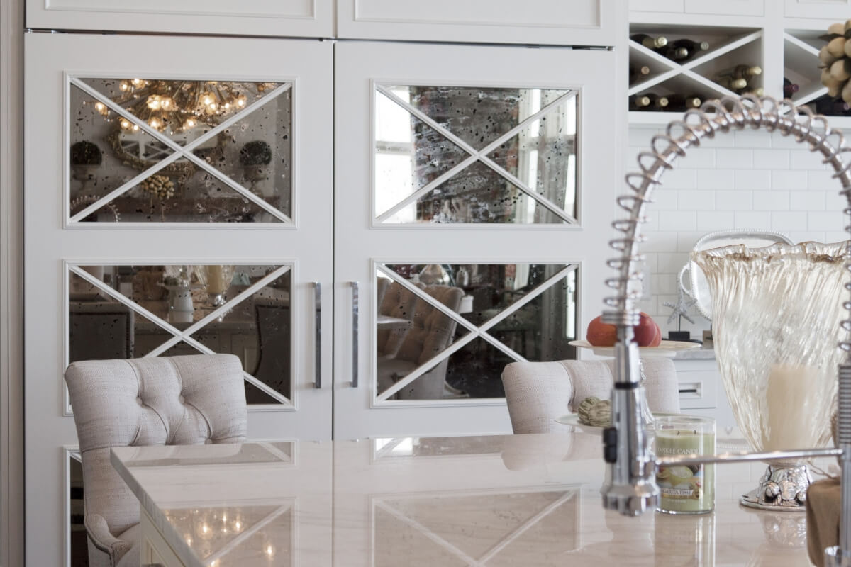 Mirrored cabinets with an X mullion cabinet door pattern. Mirrors on a large kitchen appliance, a kitchen fridge.