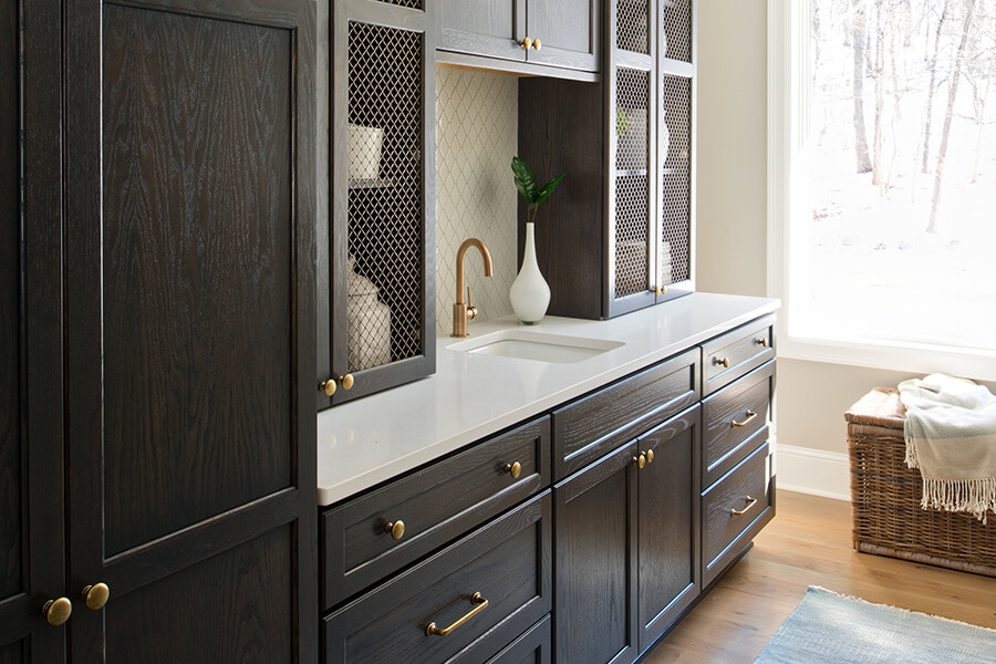 Kitchen designs are using traditional oak cabinets with a modern twist. Transitional and Contemporary designs are starting to use oak and quarter-sawn oak cabinetry with gray, true-brown, and light natural stained finishes. This dark gray stained pantry uses oak cabinets with brassy hardware.