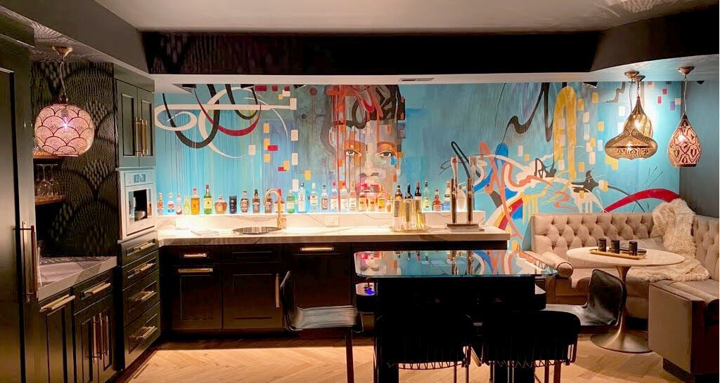 A stunning modern and trendy urban basement remodel with a dark green wet bar and bright colorful artwork.