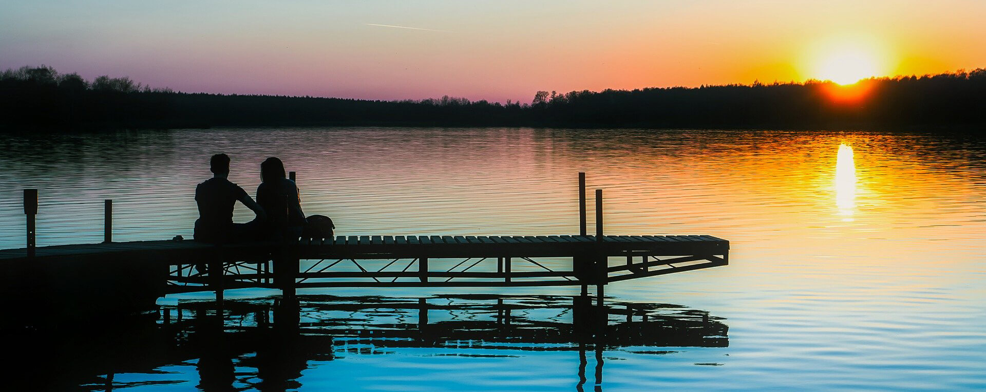 A couple sitting on the end of the dock at their lake house.