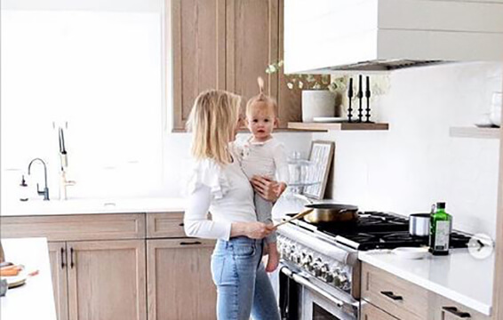 A mother holds her young toddler in their brand new kitchen with Scandi styled cabinets crafted by Dura Supreme.