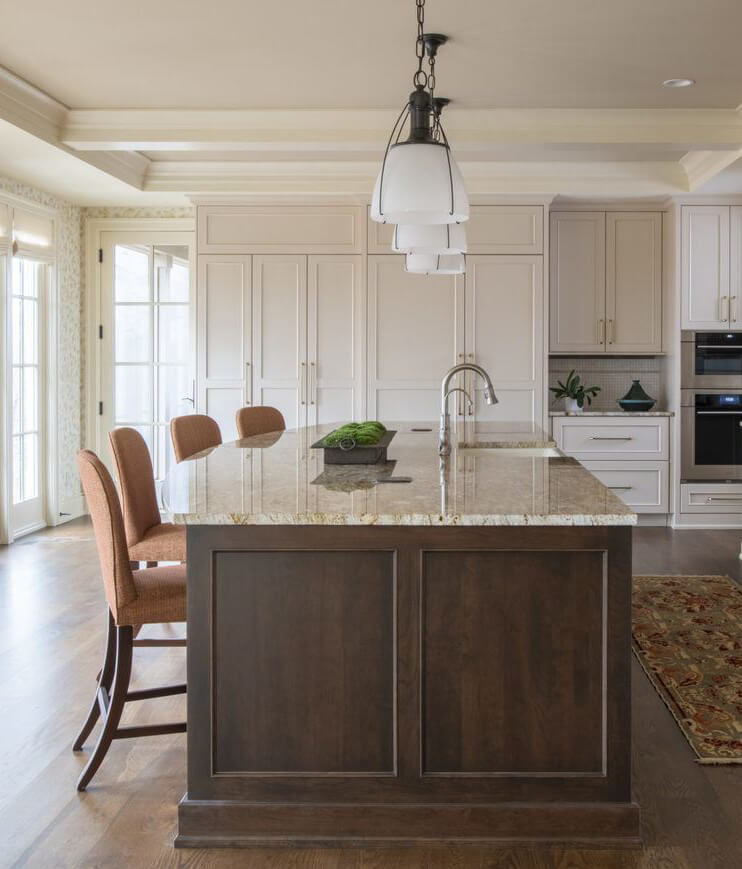 A dark stained kitchen island in a traditional white painted kitchen with counter height seating for four stools.