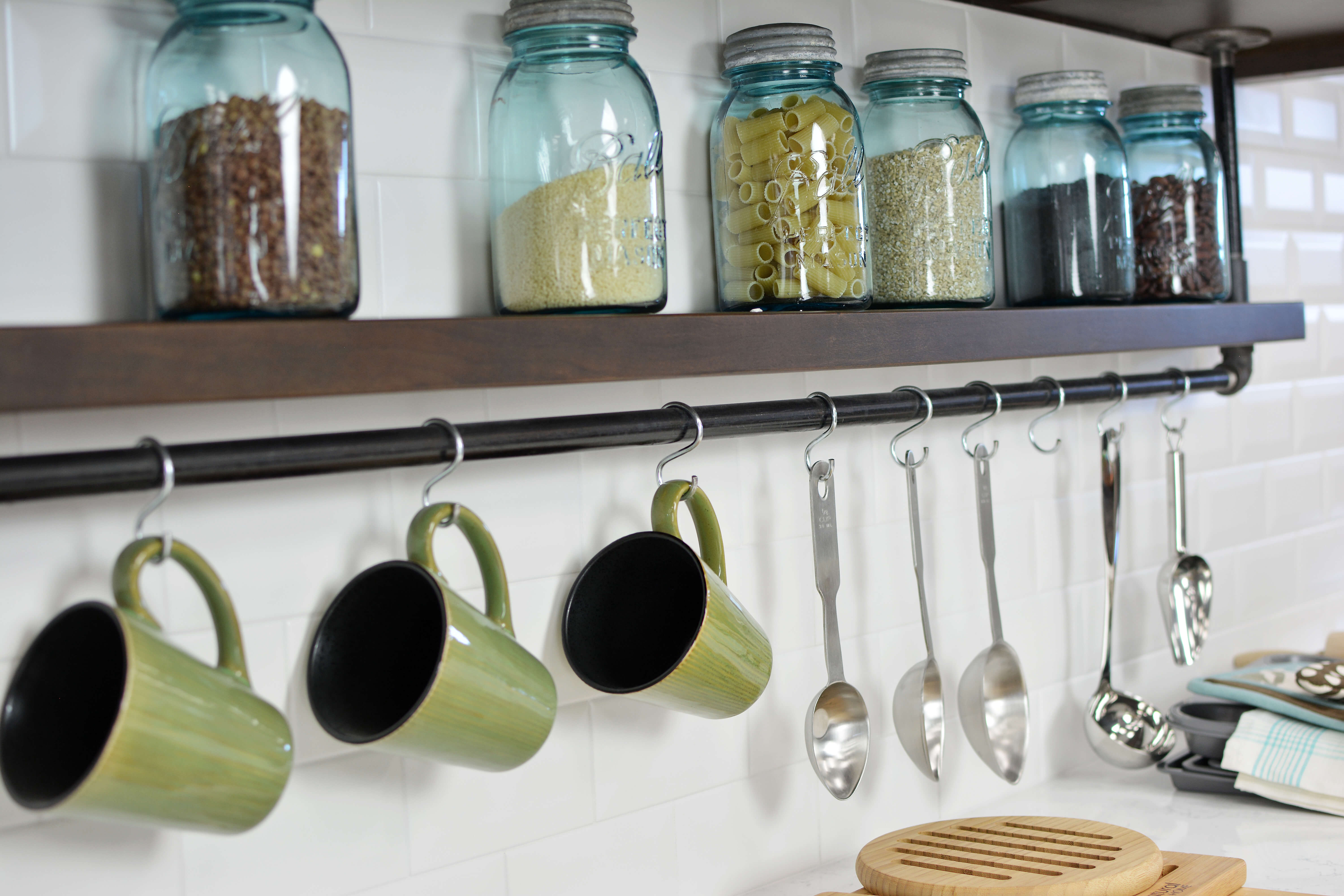 In this kitchen, an industrial style shelf hangs from the wall cabinets with hanging coffee cup storage. This feature is placed strategically within a close distance to the coffee station.