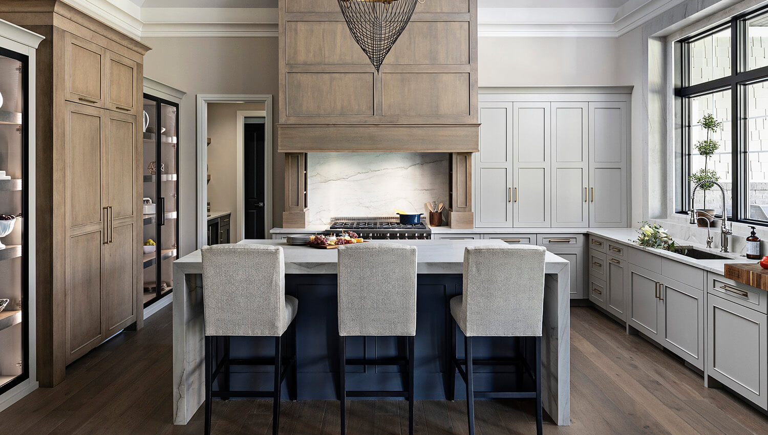 Kitchen design by KSI Kitchen & Bath, Michigan. The cabinets feature Dura Supreme's Silverton door style in the Zinc paint for the perimeter, Cyberspace blue for the kitchen island, and a true-brown Cashew stain on Maple for the grand-sized wood hood and accents. 