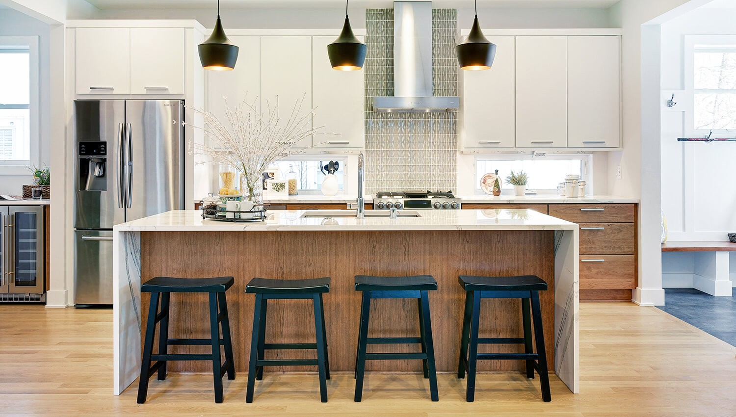 This Dura Supreme cabinetry is shown in the Toast stain on Red Oak on the kitchen island that also features a contemporary styled waterfall countertop. The perimeter cabinets are an off-white slab cabinet door with a modern look.