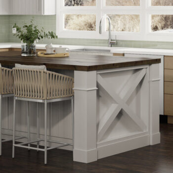 A white painted kitchen island and cabinetry capped with two grand columns with a modern farmhouse styled X patterned end cap treatment.