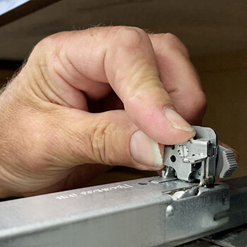 A cabinet installer adjusting the drawer glides on a kitchen drawer.