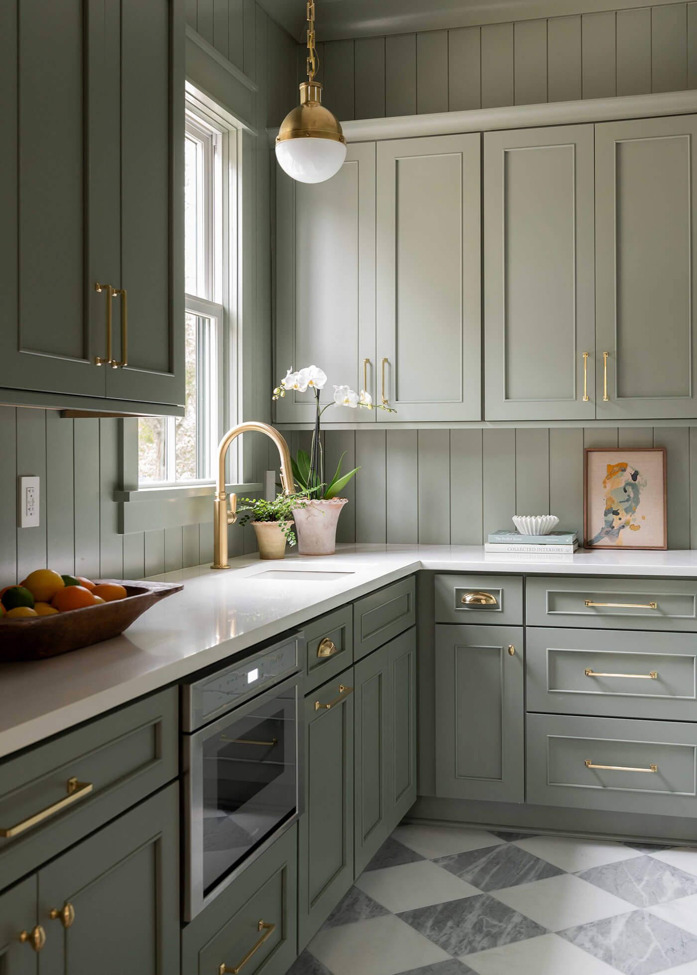 A soft sage green painted walk-in pantry space with color drenched green cabinets, walls, backsplash, and checkered floor tiles.
