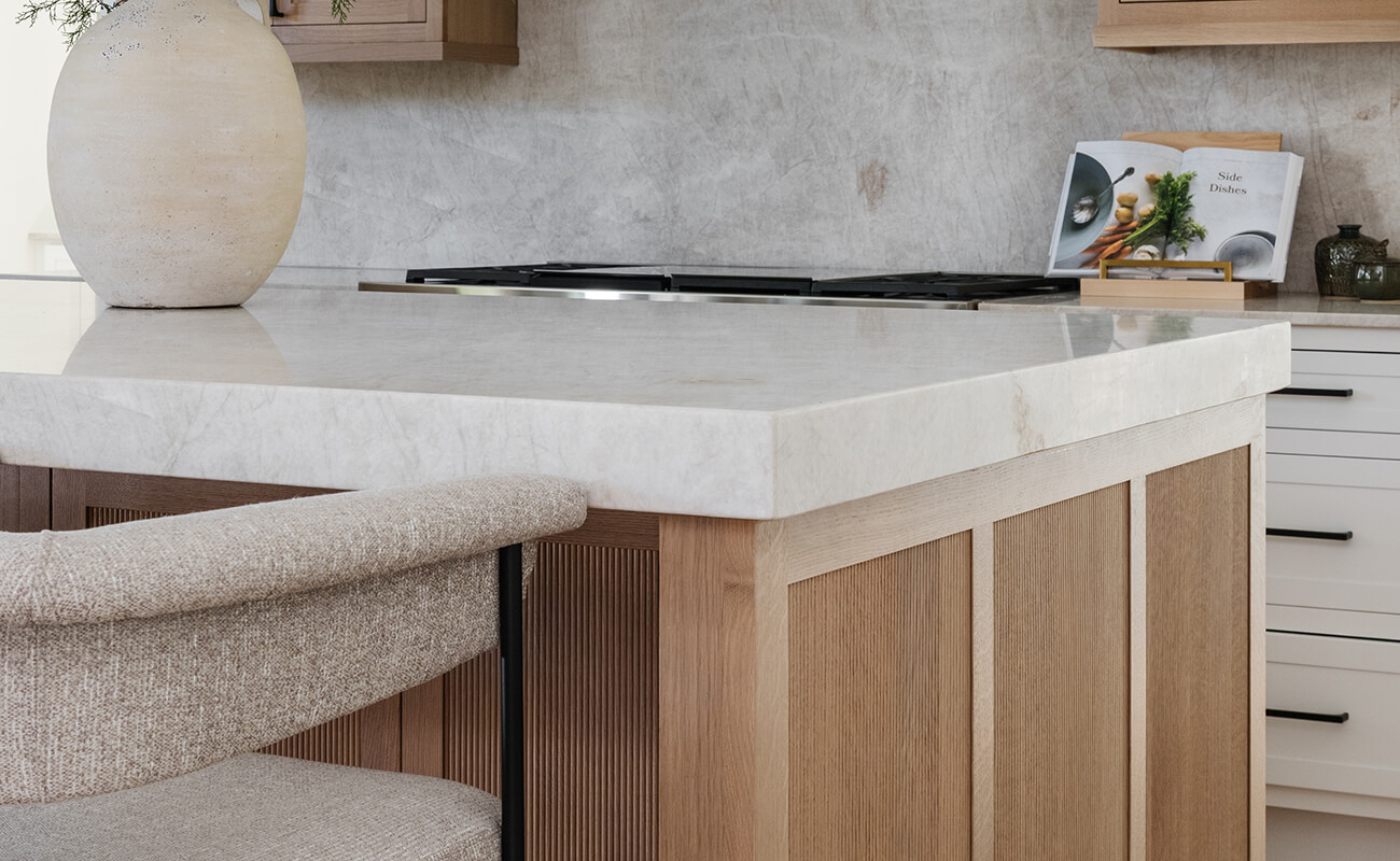 A close up of a light stained wood kitchen island with reeded panel details.